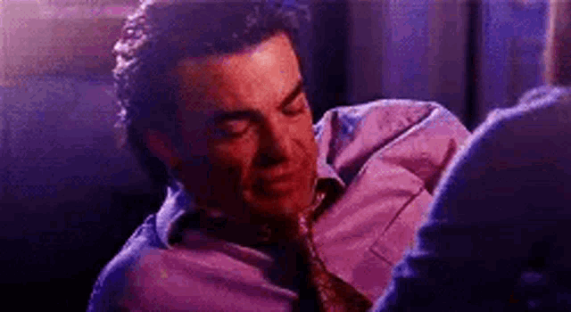 a man in a purple shirt and tie is sitting next to another man in a dark room .