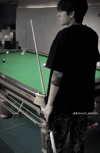 a man with a tattoo on his arm is standing in front of a pool table holding a pool cue