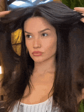 a woman with long dark hair holds her hair in her hands
