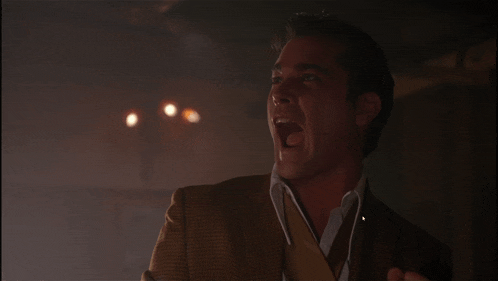 a man in a brown suit and white shirt is laughing with his mouth open