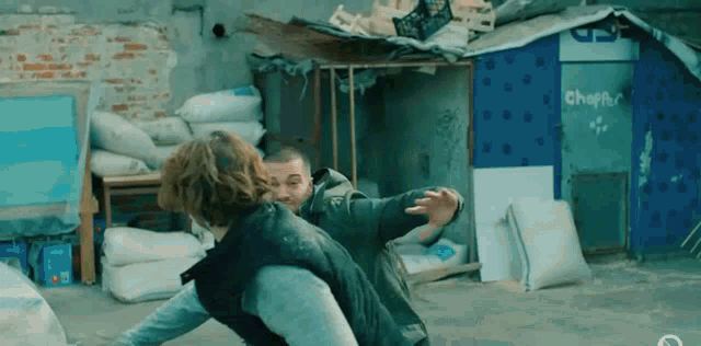 two men are fighting in front of a brick building in a slum area .