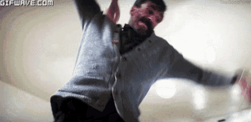 a man with blood on his face is dancing with his arms outstretched in a room .
