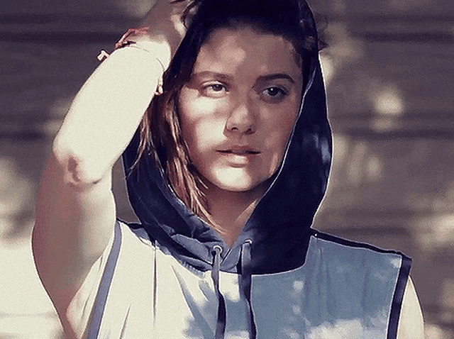 a woman wearing a blue and white hoodie holds her hand to her hair