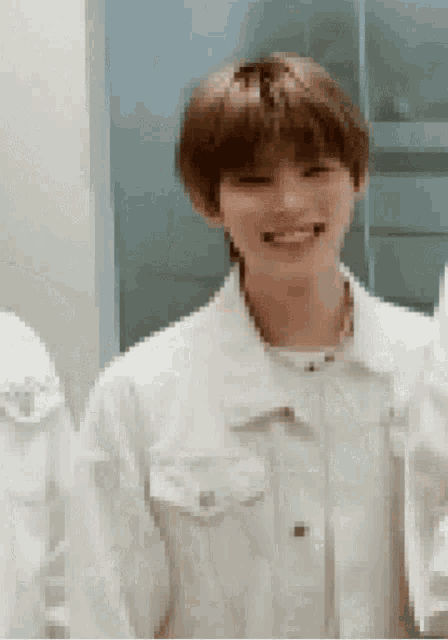 a young man in a white jacket is smiling while standing in front of a mirror .
