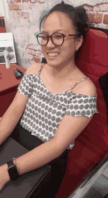 a woman wearing glasses and a patterned off the shoulder top smiles