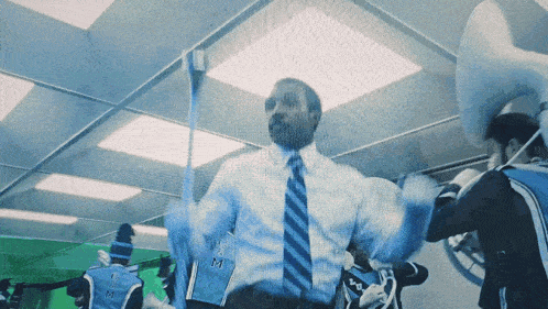 a man in a suit and tie is holding a stick with the letter m on his shirt