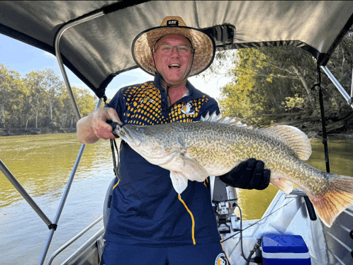 a man on a boat holding a large fish and wearing a shirt that says gfy