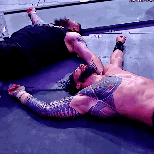 a man with a tattoo on his chest is laying on the ground next to another man with a tattoo on his arm
