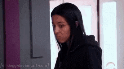 a woman with long black hair is standing in front of a door and making a funny face .