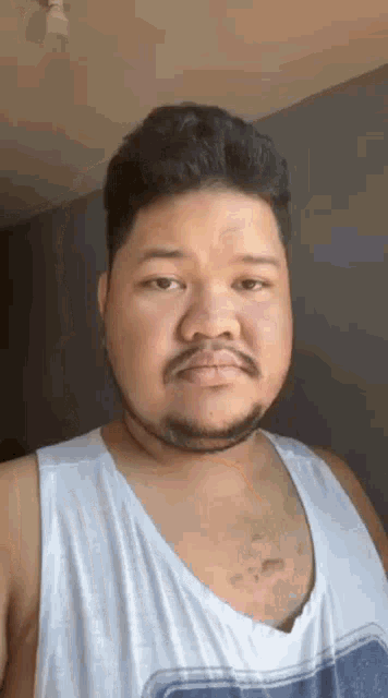a man with a beard wearing a white tank top is making a funny face .