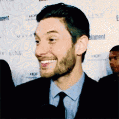 a man wearing a suit and tie is smiling in front of a wall that says entertainment