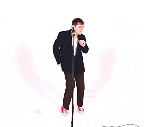 a man in a suit is singing into a microphone while wearing red sneakers
