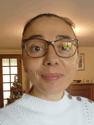 a woman wearing glasses and a white sweater is smiling