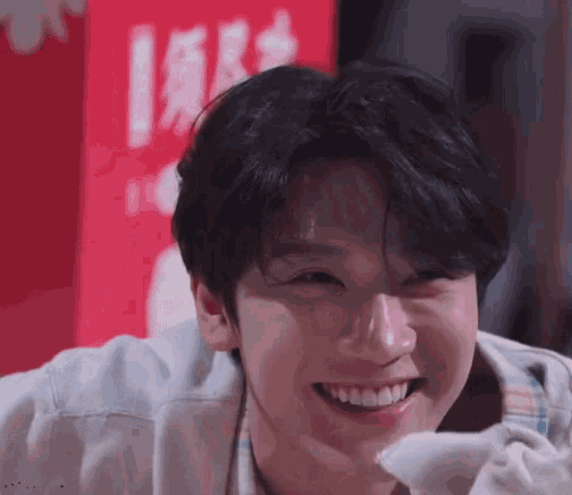 a close up of a young man smiling with his eyes closed in front of a red sign .