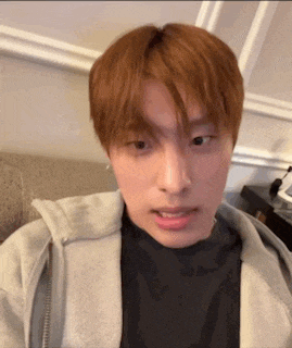 a young man with red hair is sitting on a couch wearing a gray hoodie and a black shirt .