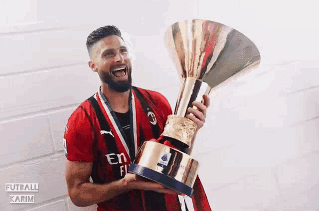 a soccer player in a fly emirates shirt holds a trophy