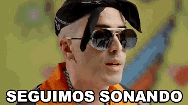 a man wearing sunglasses and a bandana with the words seguimos sonando written below him .