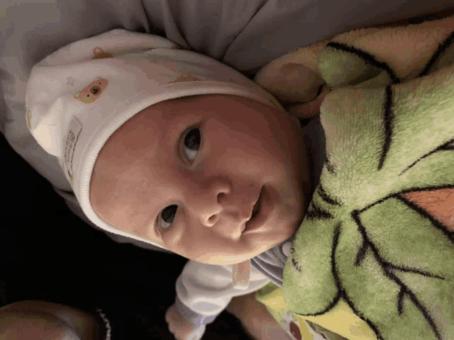 a baby wearing a white hat with a teddy bear on it looks at the camera