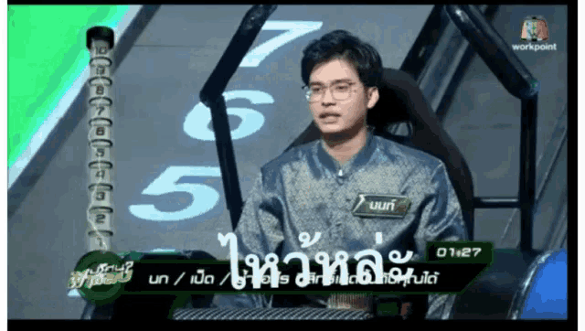 a man is sitting in front of a green screen with numbers on it
