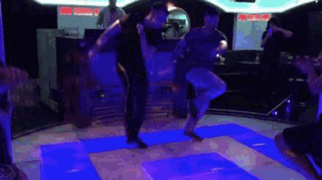 two men are dancing on a dance floor in a dark room with purple lights .