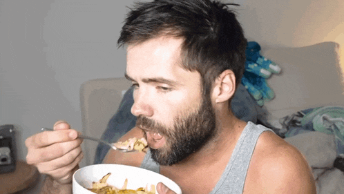 a man with a beard is eating a bowl of cereal with a spoon