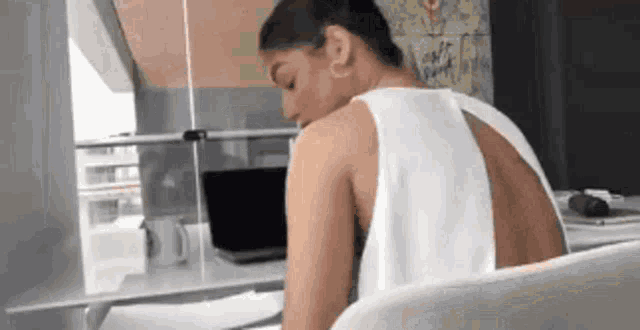a woman in a white tank top is sitting at a desk in front of a laptop .
