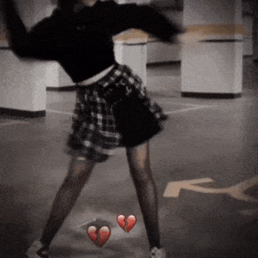 a woman in a plaid skirt is dancing in a parking garage with a broken heart in the background