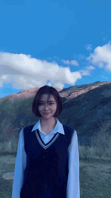 a young woman wearing a white shirt and a black vest stands in front of a mountain