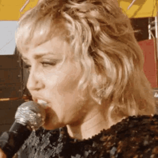 a close up of a woman singing into a microphone with her mouth open .