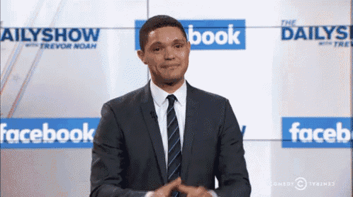 a man in a suit and tie is standing in front of a wall that says facebook