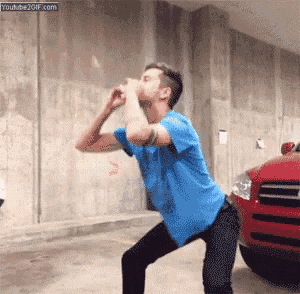 a man in a blue shirt and black pants is squatting in front of a red car .