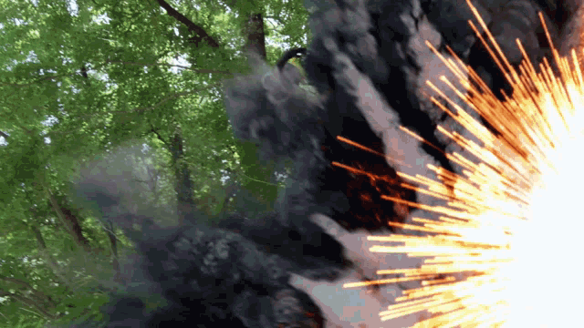 a large explosion with sparks coming out of it in front of trees