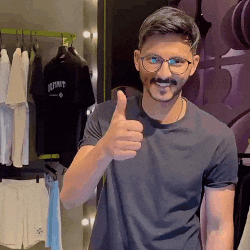 a man wearing glasses is giving a thumbs up in front of a shirt that says infinity