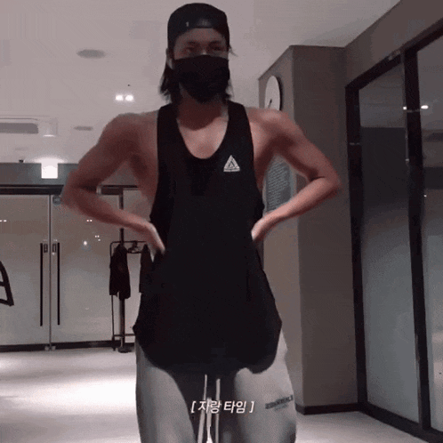 a man wearing a black adidas tank top stands in a gym with his hands on his hips