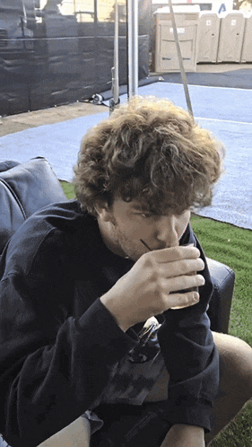 a man with curly hair is sitting on a couch drinking from a cup