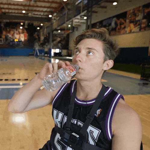 a basketball player wearing a black and purple jersey with the number 5 drinking water from a bottle