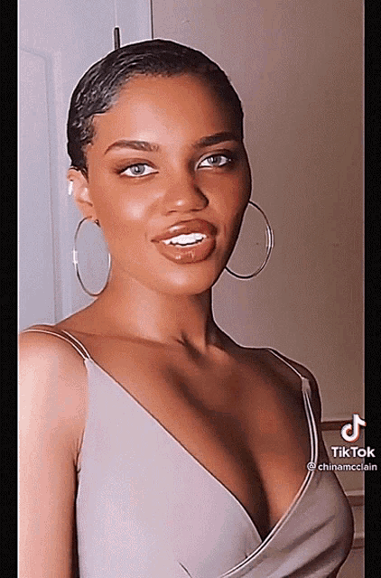 a woman wearing hoop earrings and a plunging neckline looks at the camera with tiktok written on the bottom