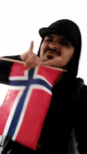 a man in a black hat is holding a small norwegian flag and giving a thumbs up