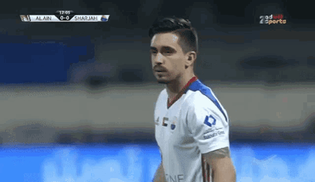 a soccer player stands on a field during a game between alain and sharjah