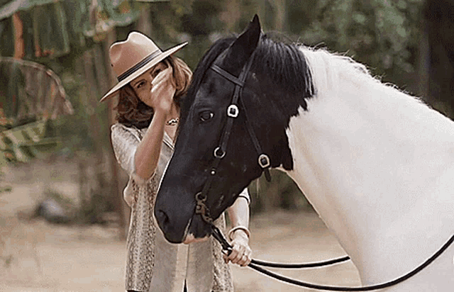 a woman in a hat is holding a black and white horse .
