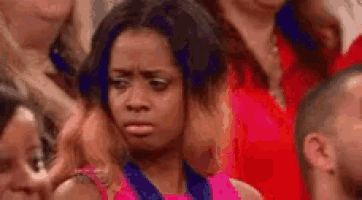 a woman in a pink shirt is sitting in a crowd of people making a funny face .
