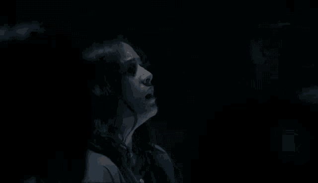 a woman is sitting in a dark room with her eyes closed and her mouth open .