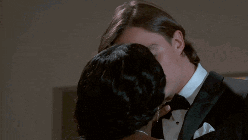 a man in a tuxedo kisses a woman in a white shirt