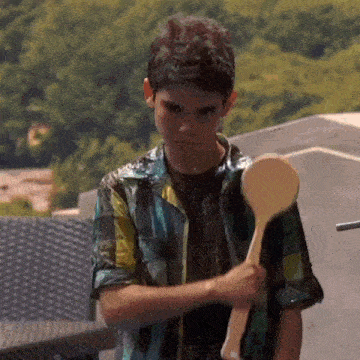 a young boy in a plaid shirt is holding a wooden spoon in his hands .