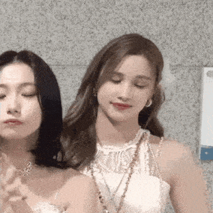 two women are standing next to each other and looking at the camera . one of the women is wearing a butterfly necklace .