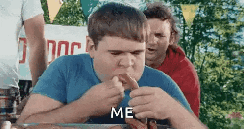 a man is eating a hot dog at a hot dog eating contest while another man watches .