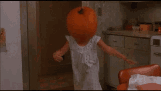 a woman is standing in a kitchen with a large orange pumpkin in the foreground