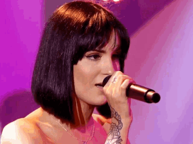 a woman is singing into a microphone with a tattoo on her arm