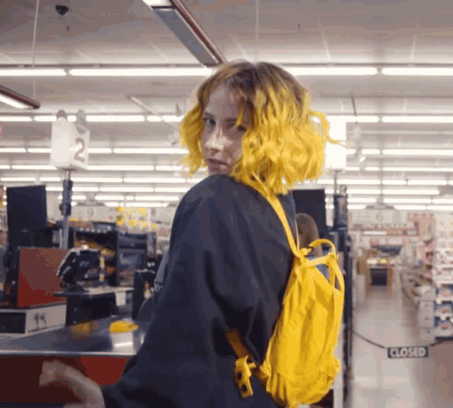 a woman with yellow hair and a yellow backpack in a store with a closed sign