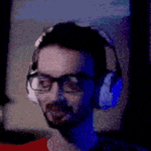 a man with glasses and headphones is sitting in front of a computer .